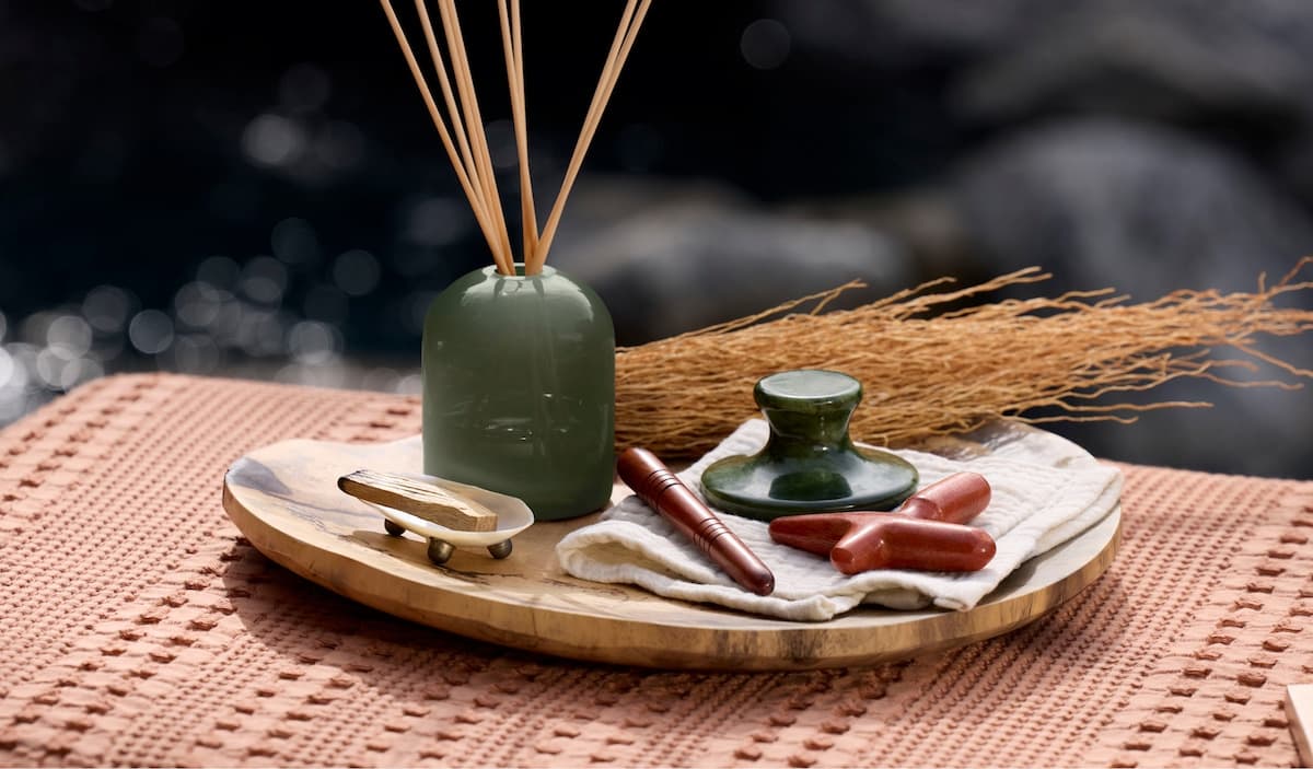 Zen setup: green diffuser with reeds, gua sha stones and massage tools on a wooden tray