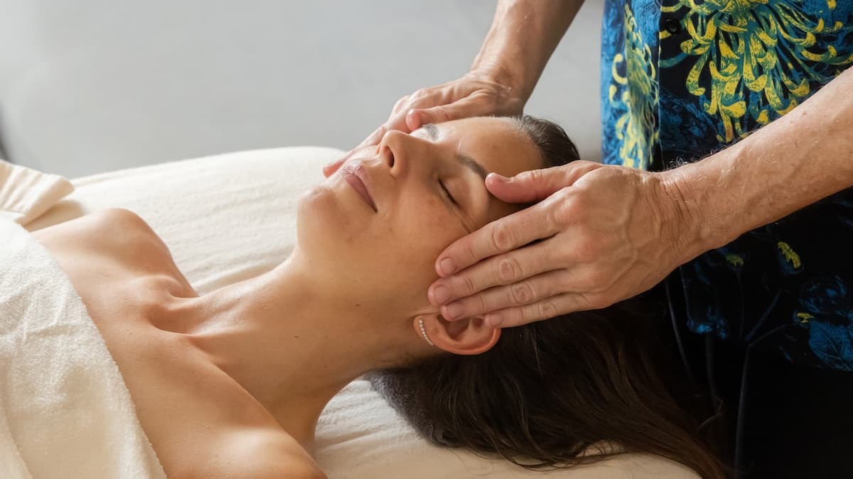 Face and temple massage on a client resting on a white pillow, relaxed expression