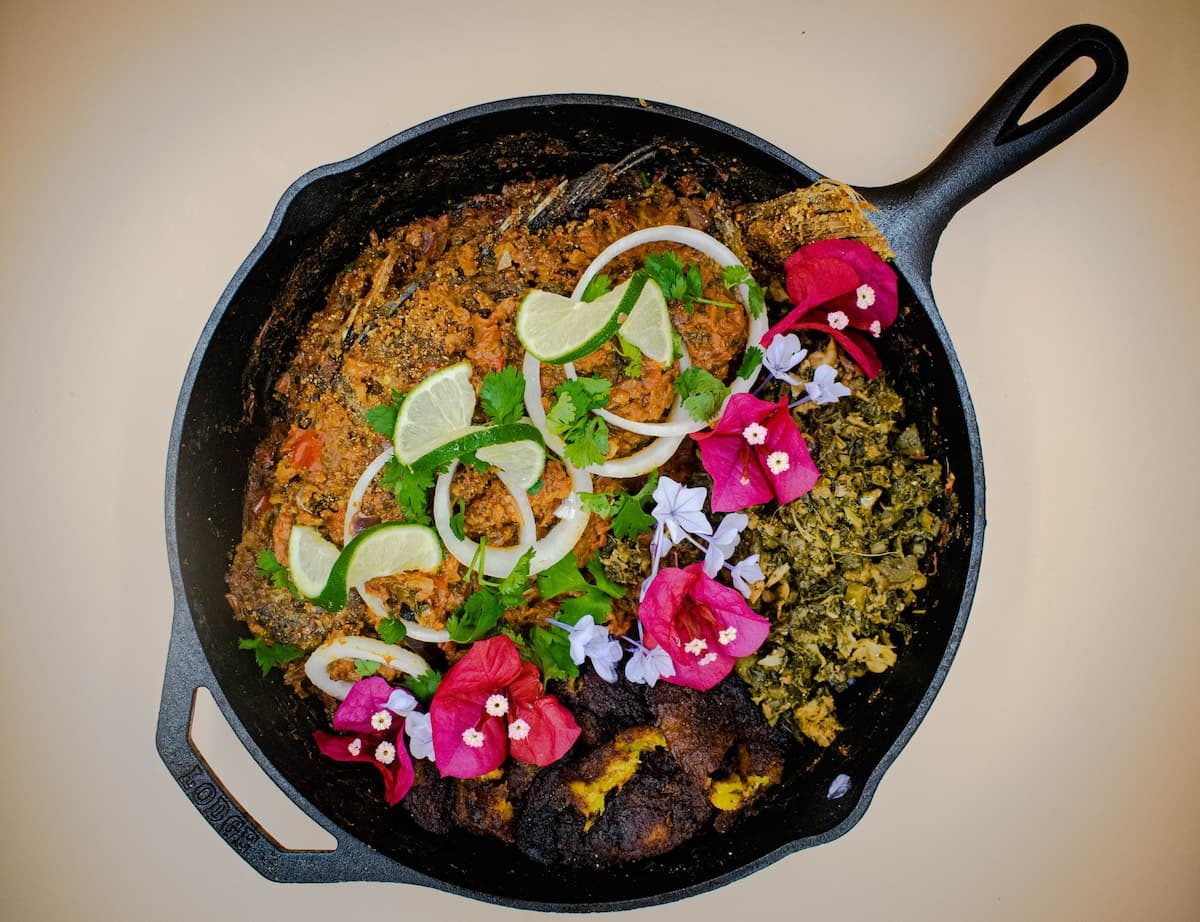 Cast-iron pan with Cali-Caribbean dish garnished with lime, onion, and bougainvillea flowers