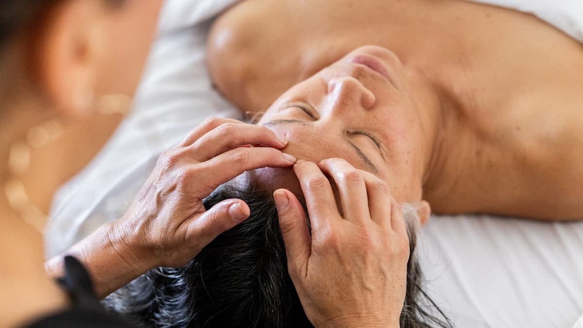 Close-up of scalp and temple massage with two hands, client's eyes closed